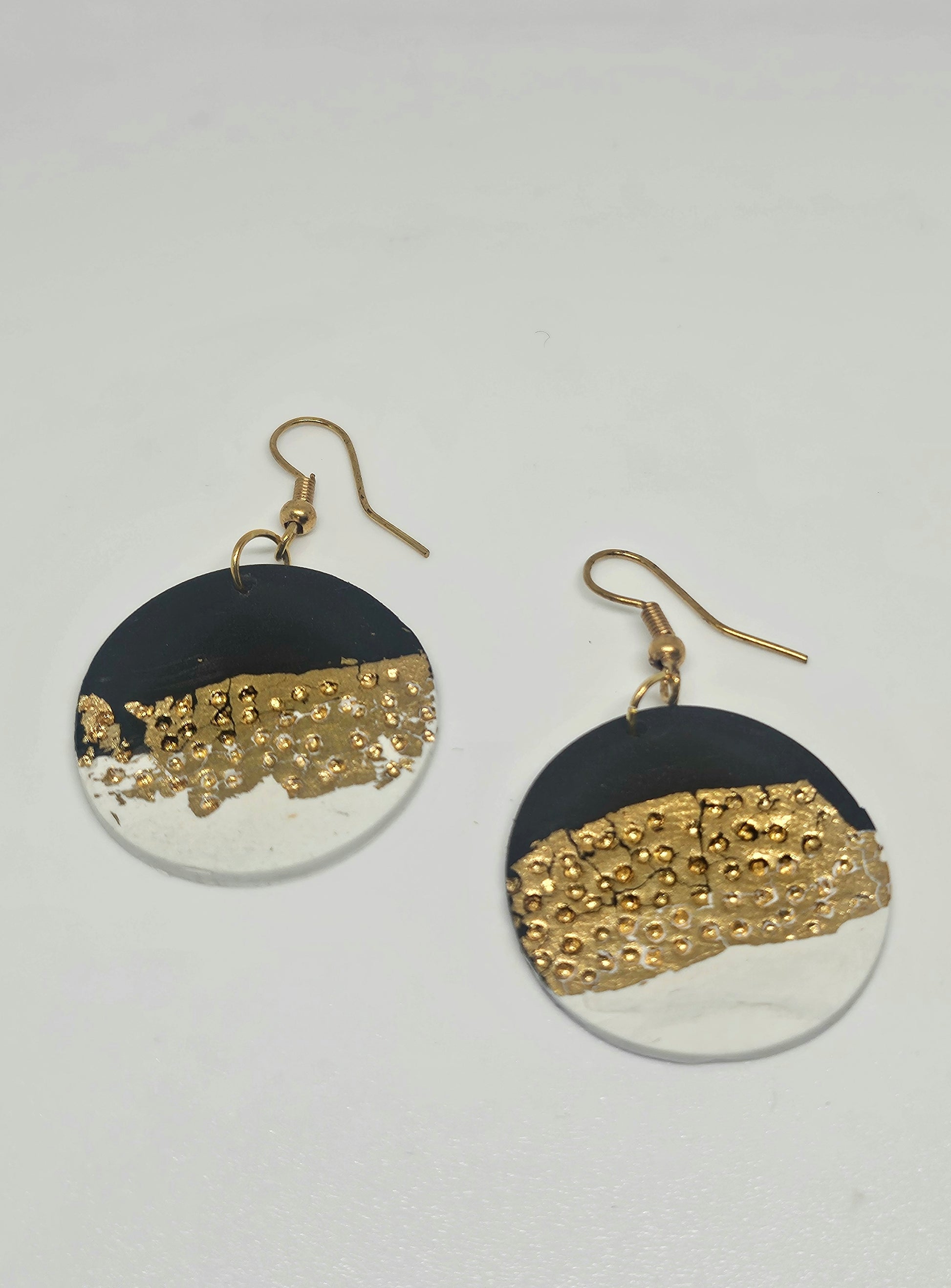 Pair of handmade polymer clay earrings with black, gold, and white design on a light gray background